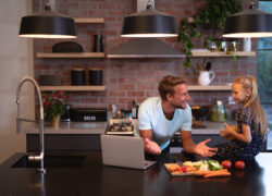 Caucasian man at home, standing by a table, using a laptop with his daughter, looking at each other, social distancing and self isolation in quarantine lockdown during coronavirus covid19 epidemic